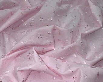 May include: Pink cotton fabric with a delicate embroidered floral pattern. The fabric is soft and lightweight, making it ideal for a variety of sewing projects.