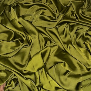 Puede incluir: Primer plano de una tela suave y sedosa de color verde oliva oscuro. La tela está drapeada y doblada, creando líneas suaves y fluidas.