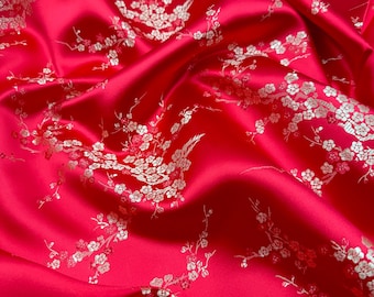 Könnte beinhalten: Roter Satin-Stoff mit einem weißen Blumenmuster. Der Stoff ist drapiert und hat einen seidigen Glanz.