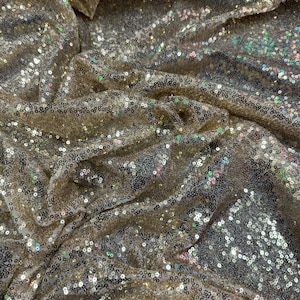 May include: Close-up of a gold sequined fabric with iridescent sequins. The fabric is wrinkled and has a soft, shimmery texture.