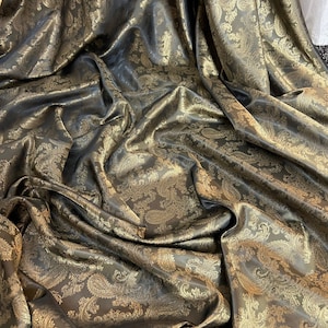 May include: A close-up of a fabric with a paisley pattern. The fabric is a dark brown colour with gold accents. The fabric is draped and folded, showing the texture and detail of the pattern.