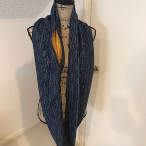 Puede incluir: Una bufanda infinita azul marino con un patrón geométrico y un forro amarillo. La bufanda se muestra en un maniquí.