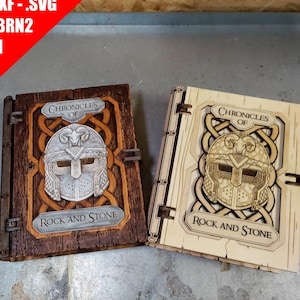 May include: Two rectangular wooden book covers featuring a laser-cut design of a horned helmet centered above the text Chronicles of Rock and Stone. One cover is dark brown wood, and the other is light beige wood, both with intricate knotwork borders.