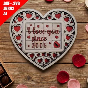 Può includere: Decorazione in legno a forma di cuore con cornice bianca e ritagli a forma di cuore rosso. Il centro presenta una cornice più piccola con le parole "I love you since 2005" in rosso. Sfondo in legno con petali di rosa sparsi.