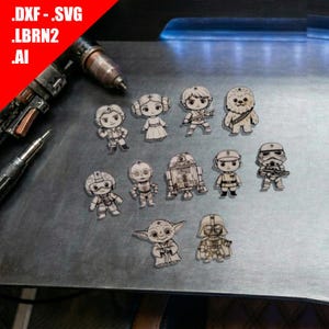Può includere: Una collezione di undici ornamenti in legno tagliati al laser raffiguranti figure stilizzate di una serie di fantascienza, tra cui un droide, un Wookiee e vari umanoidi. Il testo .DXF - .SVG .LBRN2 .AI è visibile nell'angolo.