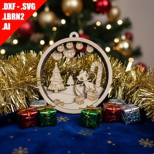 May include: Wooden Christmas ornament with a laser-cut design featuring a cat, Christmas tree, and gifts. The ornament is round with a hanging loop. Presents in red, green, and silver are at the base. Gold tinsel and a blue cloth background.