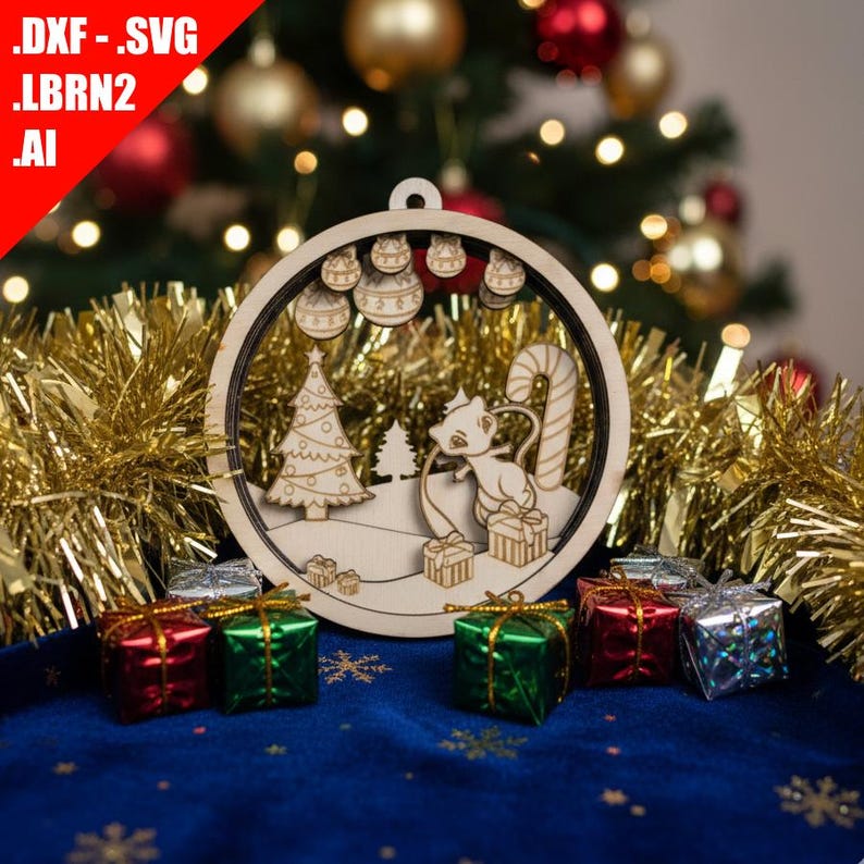 May include: Wooden Christmas ornament with a laser-cut design featuring a cat, Christmas tree, and gifts. The ornament is round with a hanging loop. Presents in red, green, and silver are at the base. Gold tinsel and a blue cloth background.