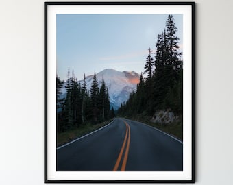 May include: A scenic photograph of a winding road leading towards a snow-capped mountain peak. The road is lined with tall evergreen trees and the sky is a soft blue with hints of pink and orange.