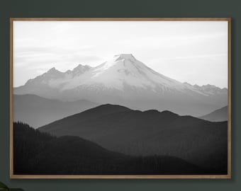 May include: A black and white photograph of a mountain range with a snow-capped peak. The photo is framed in a light wood frame and is hanging on a dark green wall.