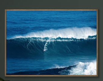 May include: A framed print of a large ocean wave, captured in shades of blue and white. The wave is breaking, with a surfer visible in the center. The artwork is displayed in a wooden frame, adding a natural touch to the scene.