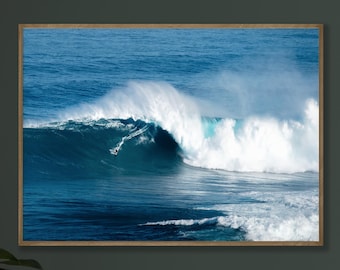 May include: A framed photograph captures a surfer riding a massive, curling ocean wave. The wave is a deep blue, with a white, foamy crest. The surfer, a small figure, is positioned on the wave's face, adding a sense of scale to the powerful scene.