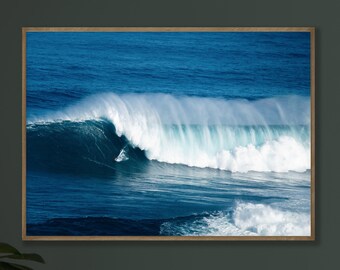 May include: A framed print of a large ocean wave, captured in a moment of breaking. The wave is a deep blue, with white foam and spray. The frame is a light brown color. The image evokes a sense of power and the beauty of nature.
