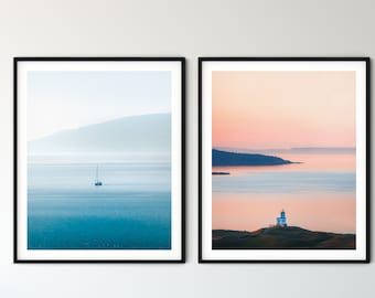 May include: Two framed landscape photographs of seascapes. The left photo shows a sailboat on a calm blue ocean with a hazy mountain range in the background. The right photo shows a lighthouse on a rocky island with a pink and orange sunset sky.