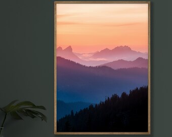 May include: A framed photograph of a mountain range at sunset. The mountains are silhouetted against a vibrant orange and pink sky. The foreground is a dark forest.