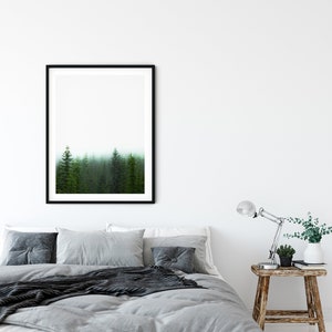May include: A gray bed with a black throw blanket and a framed print of a foggy forest above the headboard. The bed has a wooden base and is styled with gray pillows and a wooden nightstand with a lamp and a potted plant.