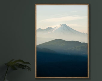 May include: A framed photograph of a snow-capped mountain peak rising above a misty forest landscape. The mountain is in the distance, with the forest in the foreground. The sky is a light blue, and the sun is shining.