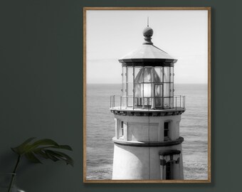 May include: A black and white photograph of a lighthouse with a large glass lens on top. The lighthouse is on a rocky coast with the ocean in the background.