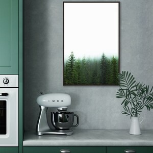 May include: A white stand mixer with a silver bowl and a black handle. The mixer is on a gray countertop in front of a green cabinet. A framed print of a foggy forest hangs on the wall behind the mixer.