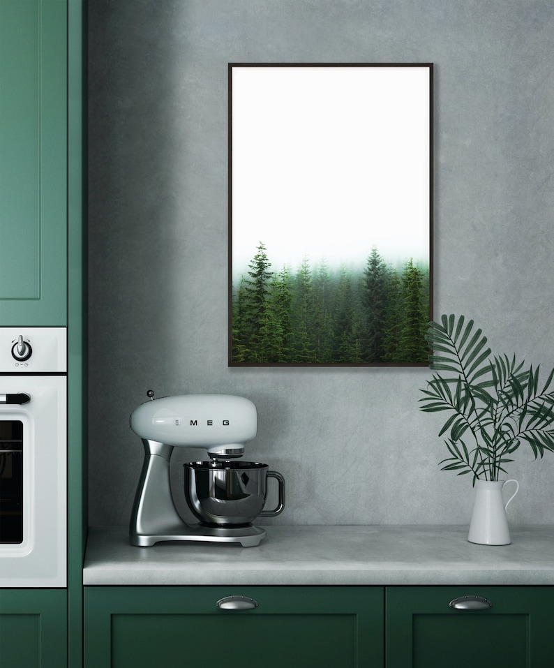 May include: A white stand mixer with a silver bowl and a black handle. The mixer is on a gray countertop in front of a green cabinet. A framed print of a foggy forest hangs on the wall behind the mixer.