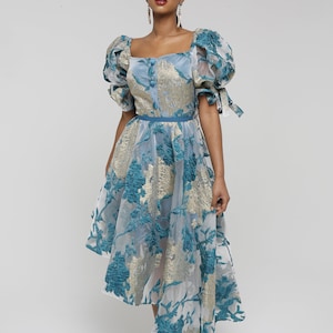 May include: A blue and gold floral patterned dress with puffed sleeves and a high neckline. The dress has a fitted bodice and a flowing skirt with a high-low hemline.