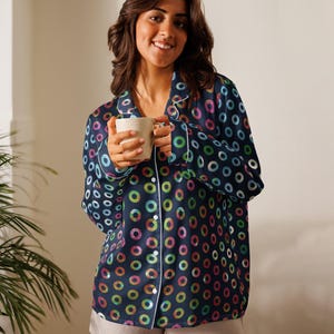 May include: Navy blue pajama set with a colorful ring pattern. The long-sleeved top has white trim and buttons down the front. The matching shorts are a light gray color. The person is holding a white mug.