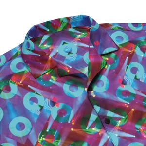 May include: A purple and blue patterned shirt with a light blue circle pattern. The shirt has a button-up collar and a button closure.