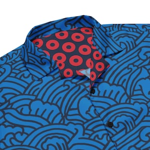 May include: A blue button-down shirt with a wave pattern in dark blue. The collar lining features a pattern of red circles on a navy background. The shirt has black buttons.