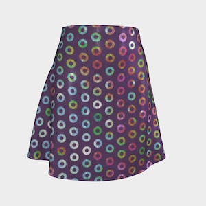 Puede incluir: Falda de línea A con un fondo morado oscuro y un patrón de círculos coloridos y brillantes. Los círculos son en tonos de azul, verde, amarillo, rosa y morado. La falda tiene una forma acampanada y una textura suave.