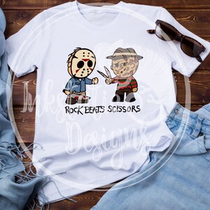 May include: White t-shirt featuring cartoon illustrations of Jason Voorhees and Freddy Krueger, with the text "Rock Beats Scissors." The design includes a hockey mask, a machete, and Freddy's glove with blades. Sunglasses and jeans are also visible.