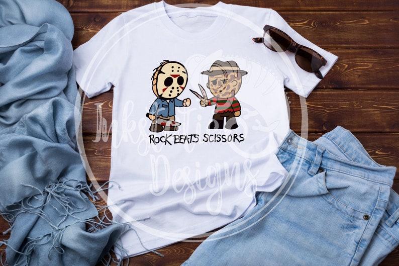 May include: White t-shirt featuring cartoon illustrations of Jason Voorhees and Freddy Krueger, with the text "Rock Beats Scissors." The design includes a hockey mask, a machete, and Freddy's glove with blades. Sunglasses and jeans are also visible.