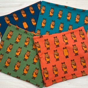 Könnte beinhalten: Vier Stoff-Halswärmer mit einem sich wiederholenden Muster aus orangefarbenen Comicfiguren mit braunen Augen und Armen. Die Halswärmer sind in den Farben Türkis, Marineblau, Grün und Orange.