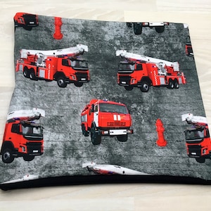 Könnte beinhalten: Roter Feuerwehrwagen mit Leitern auf einem grau-weißen gemusterten Stoff. Der Stoff hat einen schwarzen Rand.