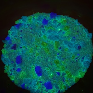 May include: Close-up of a green and blue rock with a rough, textured surface. The rock is illuminated with a bright light, highlighting its intricate details.