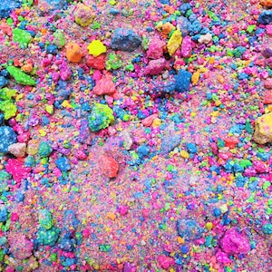 May include: A close-up of a pile of colourful, crushed, and glittery rocks. The rocks are a variety of colours, including pink, blue, green, yellow, and orange.