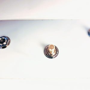 May include: Close-up of three metal hardware pieces. Two are silver-coloured with a hexagonal shape, and one has a gold-coloured top. All are set against a bright white background, creating a clean, minimalist aesthetic.