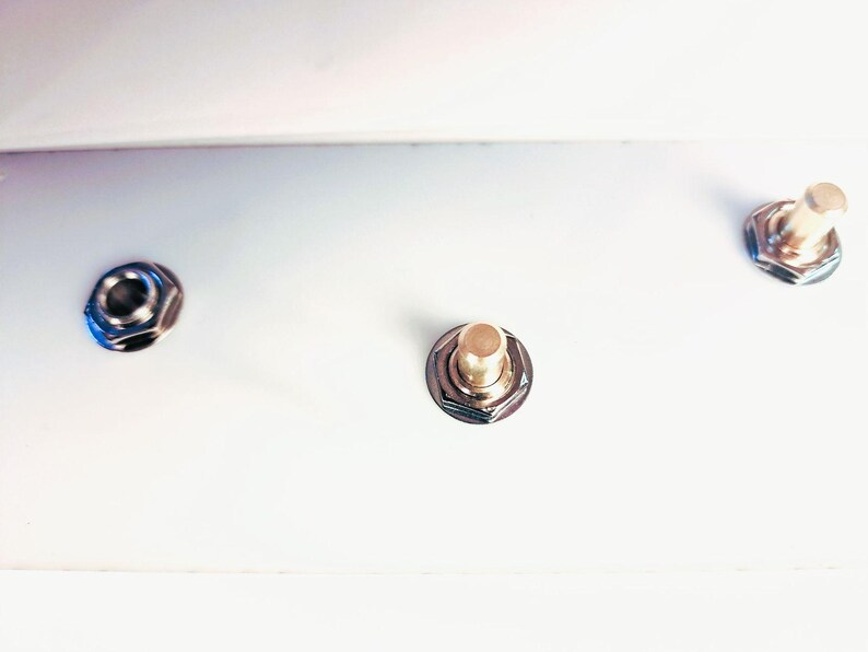 May include: Close-up of three metal hardware pieces. Two are silver-coloured with a hexagonal shape, and one has a gold-coloured top. All are set against a bright white background, creating a clean, minimalist aesthetic.