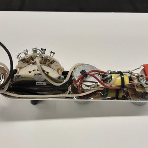 May include: A chrome guitar control plate with various electronic components, including a switch, potentiometers, capacitors, and wiring. The components are connected with wires of different colors, and the plate has three control knobs.