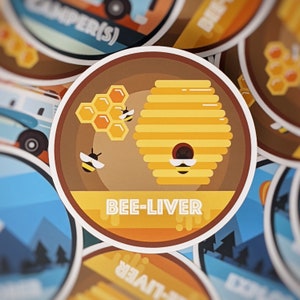 Könnte beinhalten: Ein gelber und brauner Bienenstock mit einem Wabenmuster und zwei Bienen auf jeder Seite. Der Text "BEE-LIVER" ist unter dem Bienenstock gedruckt. Das Bild ist ein Aufkleber mit einem braunen Rand.