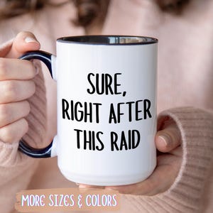 Könnte beinhalten: Weißer Keramikbecher mit schwarzem Innenraum und Henkel, mit dem Text "Sure, Right After This Raid" in Schwarz. Der Becher wird von einer Person gehalten, die einen rosa Pullover trägt. Der Becher hat die Worte "More Sizes & Colors" am unteren Rand.