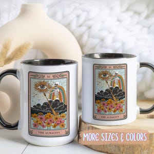 Two white ceramic mugs with black handles and rims. Each mug features a tarot card design with a skeleton, rainbow, and flowers. The text "THE AUDACITY" is printed on the bottom of the card. Gift for him. Gift for her. Birthday gift. Christmas present. 11oz and 15oz, several colors. Unique custom made coffee mug. Best friend mugs. Coffee lover. Secret santa. Coworker gift exchange. Stocking stuffer. White elephant. Novelty cup Dishwasher safe & microwave safe