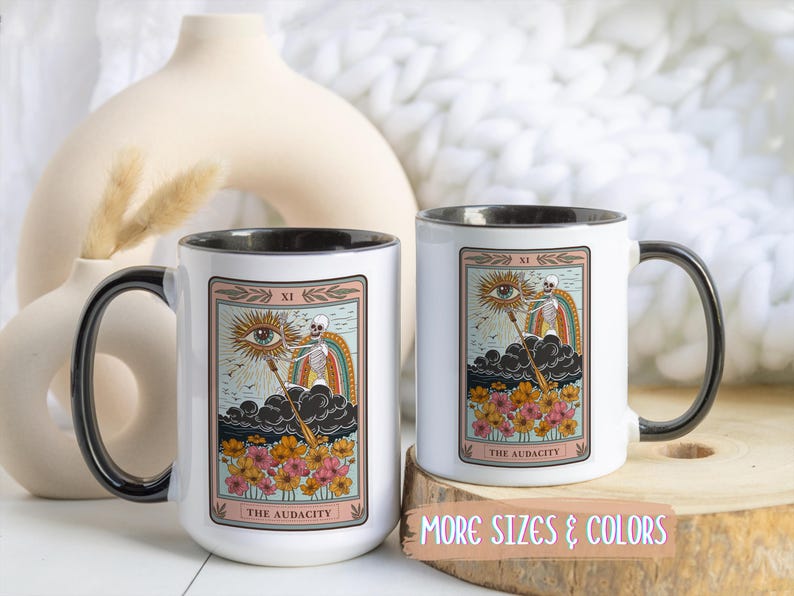 Two white ceramic mugs with black handles and rims. Each mug features a tarot card design with a skeleton, rainbow, and flowers. The text "THE AUDACITY" is printed on the bottom of the card. Gift for him. Gift for her. Birthday gift. Christmas present. 11oz and 15oz, several colors. Unique custom made coffee mug. Best friend mugs. Coffee lover. Secret santa. Coworker gift exchange. Stocking stuffer. White elephant. Novelty cup Dishwasher safe & microwave safe