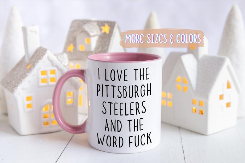 White ceramic mug with a pink interior and handle. The mug features the text "I LOVE THE PITTSBURGH STEELERS AND THE WORD FUCK" in black.