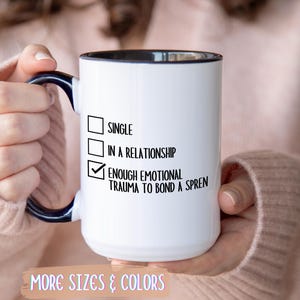 May include: White ceramic mug with a black interior and handle, featuring the text "SINGLE", "IN A RELATIONSHIP", and "ENOUGH EMOTIONAL TRAUMA TO BOND A SPREN". The mug also includes the text "MORE SIZES & COLORS".