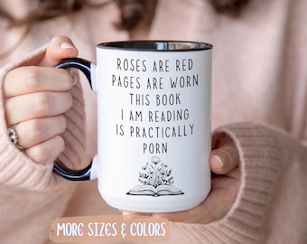 May include: White ceramic mug with a black interior and handle, featuring the text "ROSES ARE RED PAGES ARE WORN THIS BOOK I AM READING IS PRACTICALLY PORN" and an illustration of an open book with flowers. The mug also has the text "MORE SIZES & COLORS".