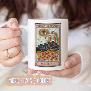 White ceramic mug featuring a tarot card design with a skeleton, eye, and rainbow. The card reads "THE AUDACITY" in a decorative frame with floral accents. Gift for him. Gift for her. Birthday gift. Christmas present. 11oz and 15oz, several colors. Unique custom made coffee mug. Best friend mugs. Coffee lover. Secret santa. Coworker gift exchange. Stocking stuffer. White elephant. Novelty cup Dishwasher safe & microwave safe