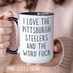 White ceramic mug with black interior and handle, featuring the text "I LOVE THE PITTSBURGH STEELERS AND THE WORD FUCK" in black.