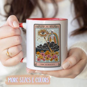 White ceramic mug with a red interior and handle. The mug features a tarot card design with a skeleton, rainbow, and flowers. The text "THE AUDACITY" is at the bottom of the card. Gift for him. Gift for her. Birthday gift. Christmas present. 11oz and 15oz, several colors. Unique custom made coffee mug. Best friend mugs. Coffee lover. Secret santa. Coworker gift exchange. Stocking stuffer. White elephant. Novelty cup Dishwasher safe & microwave safe