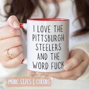 White ceramic mug with a red interior and handle. The mug features the text "I LOVE THE PITTSBURGH STEELERS AND THE WORD FUCK" in black.