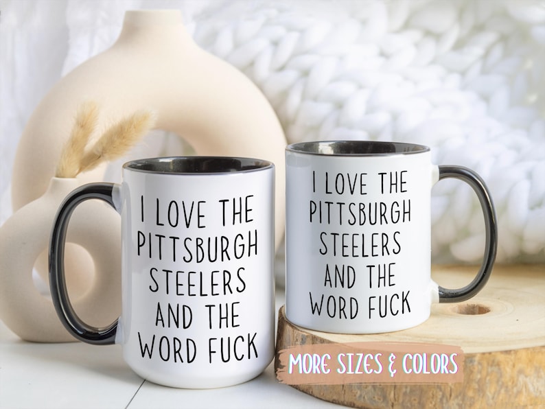 Two white ceramic mugs with black handles and rims. Each mug has the text "I LOVE THE PITTSBURGH STEELERS AND THE WORD FUCK" printed in black.