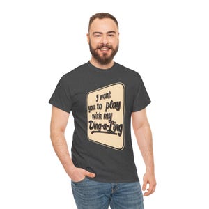 May include: Dark grey t-shirt featuring the text "I want you to play with my Ding-a-Ling" in a retro design. The text is black, set against a cream background with a brown border. The shirt is made of a soft material.